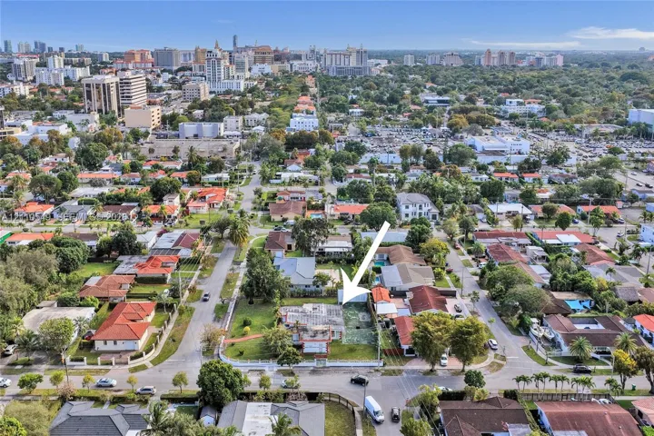 Aerial perspective of a corner lot featuring a residential structure, expansive lawn, mature landscaping, and a fenced perimeter
