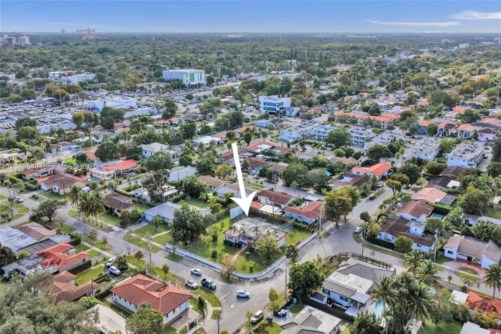Corner-lot property featuring a multi-pitched roof, paved driveway, mature perimeter landscaping, and a central lawn area