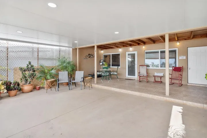 Covered outdoor patio featuring a concrete floor, recessed lighting, exposed wood ceiling beams, and white lattice privacy screening