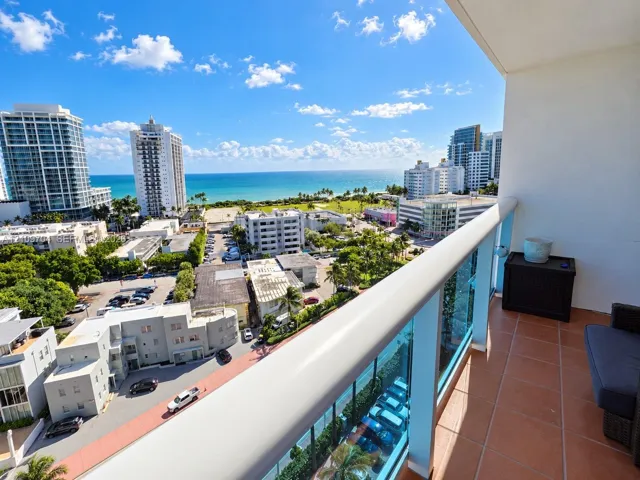 Covered balcony featuring terracotta-style tile flooring and a glass-panel railing overlooking the ocean and urban coastline