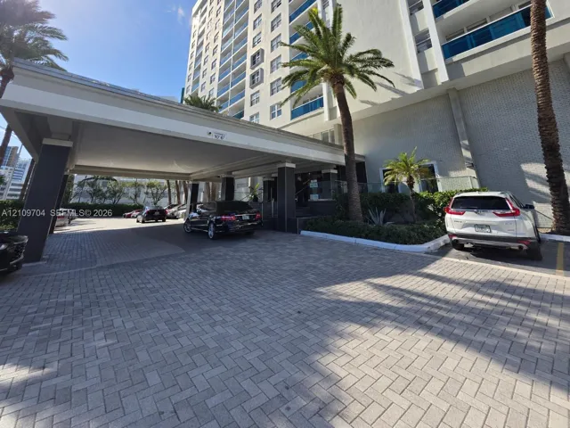 High-rise exterior featuring a paved porte-cochère, covered drop-off area, multi-story facade with glass railings, and mature palm trees