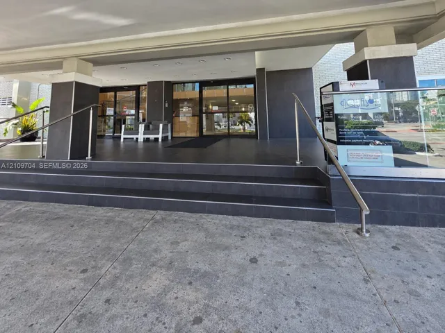 Covered building entrance featuring tiered stone steps, matte dark tile finishes, and stainless steel handrails