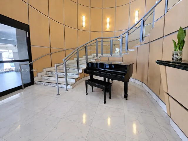 Curved staircase featuring stone treads, glass railings with metal handrails, polished tile flooring, and paneled wall finishes with integrated wall-mounted lighting