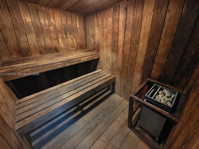 Custom sauna featuring tongue-and-groove wood paneling, multi-level slatted wood benches, and a built-in electric rock heater