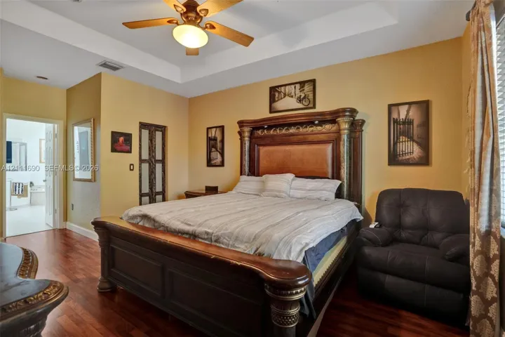 Tray ceiling, wood-finish flooring, ceiling fan with integrated light fixture, and paneled door
