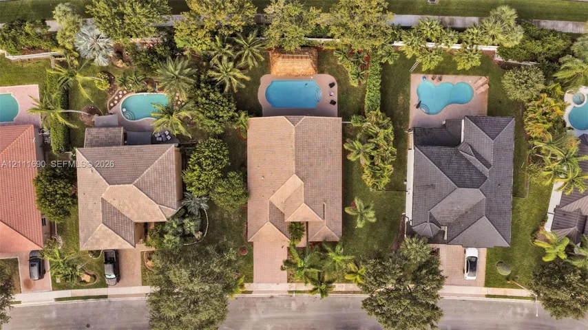 Aerial perspective featuring a shingle-roofed residence, a private swimming pool, paved driveway, and mature landscaping