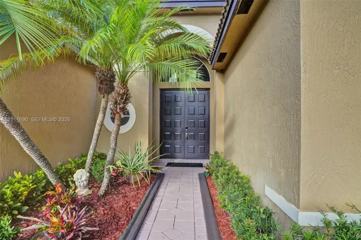Stucco exterior entry featuring double panel doors, arched transom window, and a paved walkway