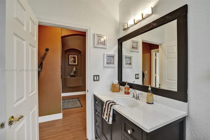Bathroom vanity featuring a solid surface countertop, undermount sink, dark-finish cabinetry, framed wall mirror, and modern multi-bulb light fixture