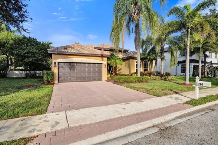 Stucco exterior featuring a multi-hipped tile roof, paved driveway, attached two-car garage, and established palm trees