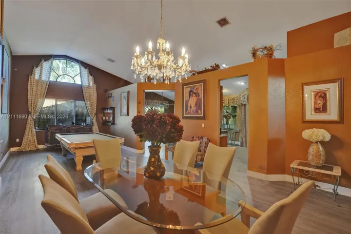 Vaulted ceilings, crystal chandelier, arched window with decorative molding, and wood-finish flooring