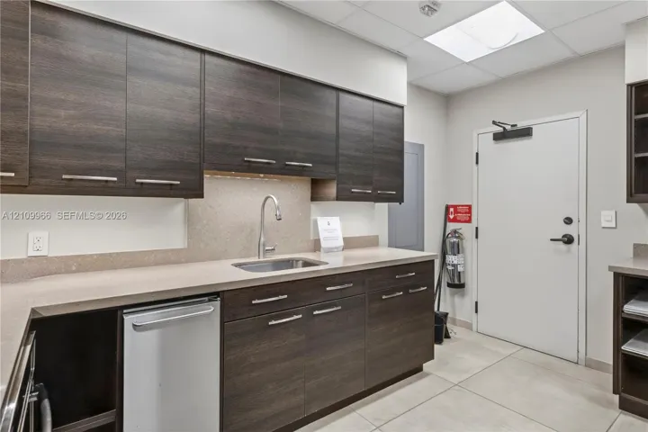 Kitchen area featuring dark wood-finish cabinetry, solid surface countertops, stainless steel undermount sink with gooseneck faucet, and tile flooring