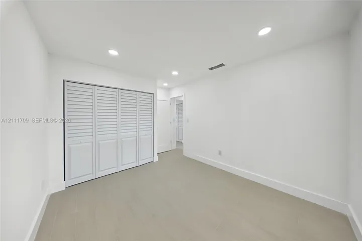 Neutral interior room featuring neutral-tone tile flooring, recessed ceiling lighting, and a multi-panel closet with louvered doors