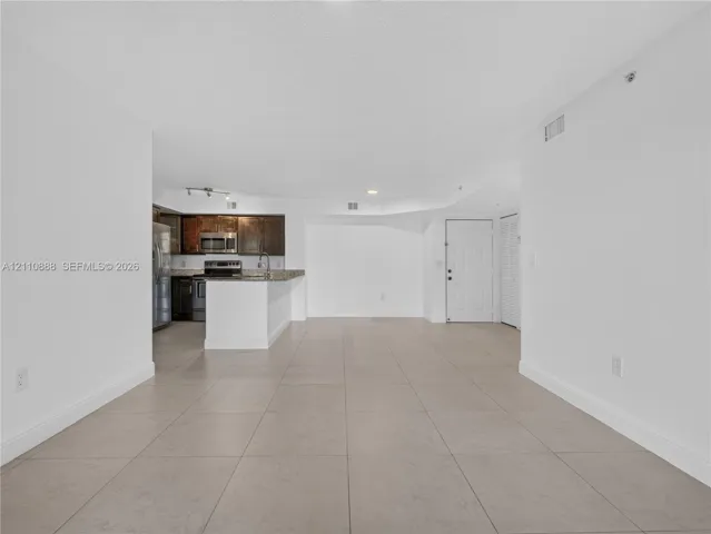 Open floor plan featuring large-format ceramic tile flooring, kitchen with dark cabinetry, stone-surface countertops, stainless steel appliances, and louvered closet doors