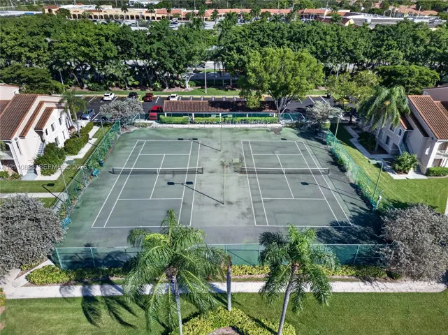 Dual outdoor tennis courts enclosed by chain-link fencing, surrounded by landscaped grounds and mature trees