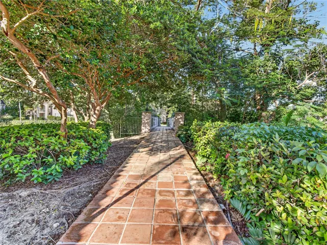 Terra cotta tile walkway framed by mature landscaping and metal fencing