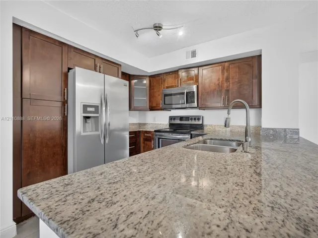Kitchen featuring dark wood-finish cabinetry, stone countertops, stainless steel appliances, a dual-basin undermount sink with a gooseneck faucet, and track lighting