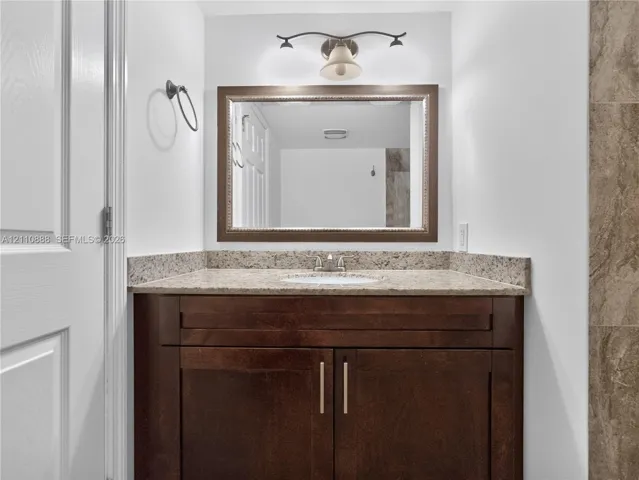 Dark wood cabinetry vanity with stone-finish countertop, integrated sink, framed wall mirror, and dual-bulb vanity lighting