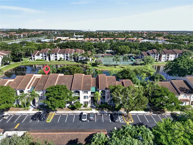 Multi-story building featuring a tile roof, waterfront positioning, mature landscaping, and hardscaped surface parking