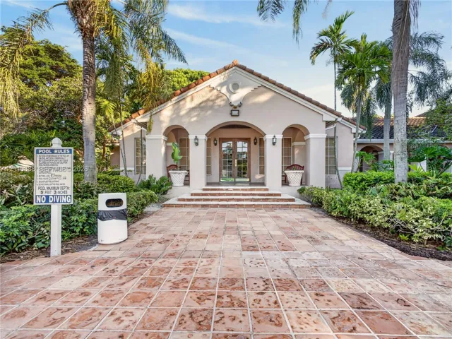 Stucco exterior featuring an arched entryway with masonry steps, stone-tile paving, and mature palms