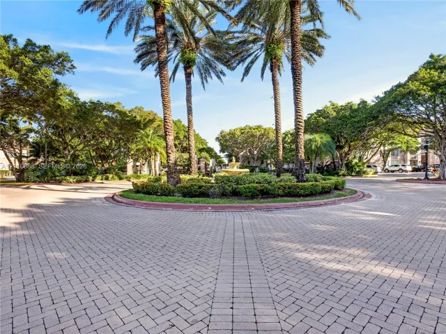 Paver brick circular drive featuring a central garden island, mature palm trees, a tiered stone fountain, and sculpted shrubbery