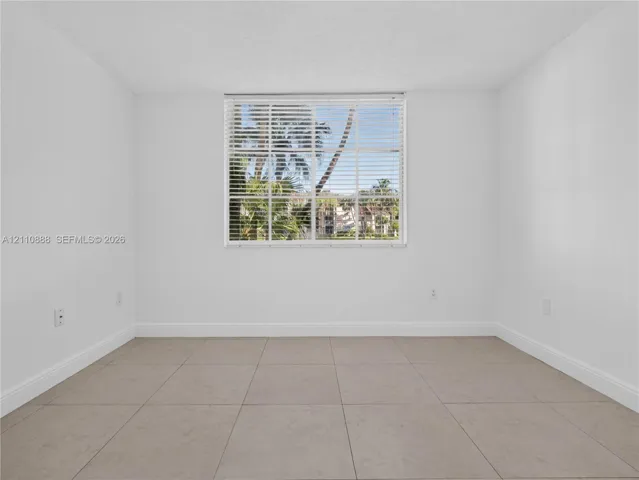 Neutral-toned ceramic tile flooring, clean white walls, and a large window with horizontal blinds