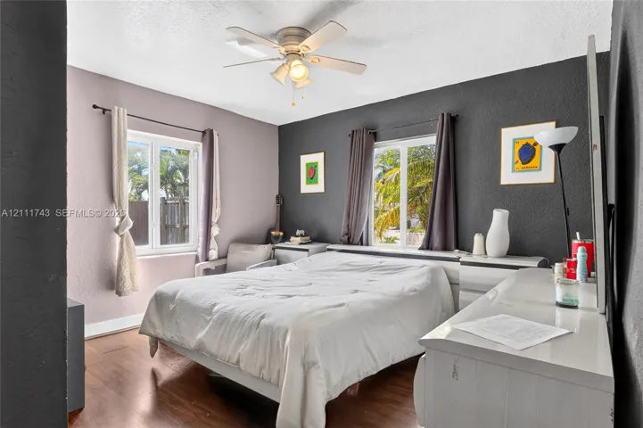 Wood-finish flooring, dual windows with deep-set frames, and a ceiling-mounted light fixture with a multi-blade fan