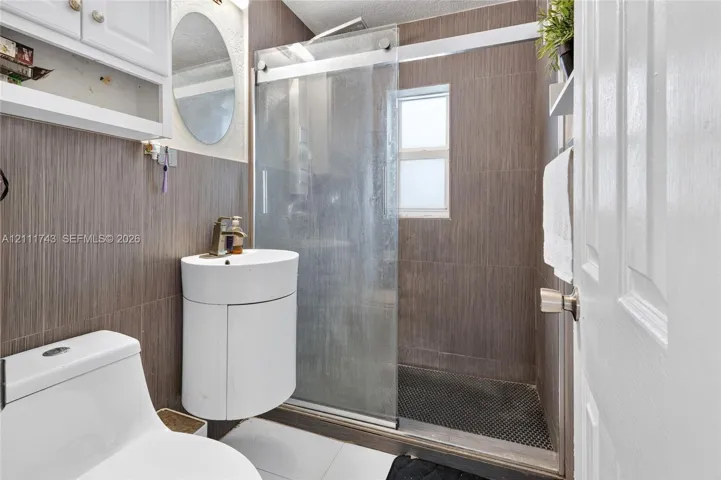 Bathroom featuring vertical wood-finish wall tile, a semi-circular pedestal sink with a metallic faucet, and a shower enclosure with a glass sliding door