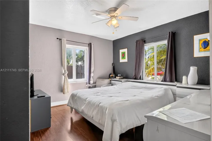 Room featuring wood-finish flooring, dual-tone painted walls, two multi-pane windows, and a central ceiling fan with an integrated light fixture