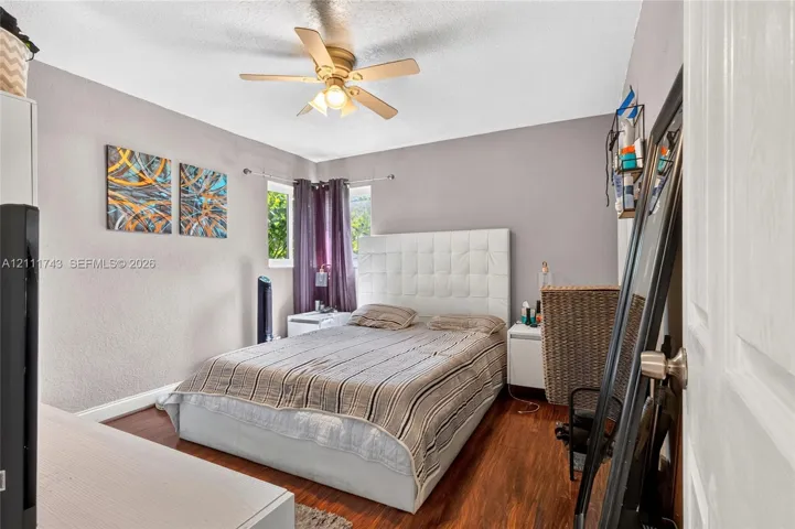 Bedroom featuring wood-finish flooring, a ceiling fan with integrated lighting, dual windows, and textured wall finish