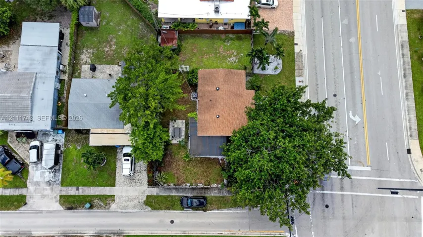 Aerial perspective of residential property featuring a shingle roof, mature landscaping, paved driveway, and grass lawn area
