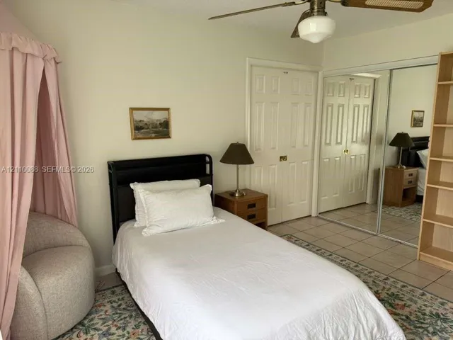 Room featuring neutral-toned tile flooring, dual-panel closet doors, mirrored wardrobe sliding doors, and a ceiling fan with integrated lighting