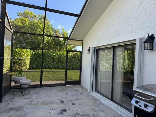 Screened-in lanai featuring concrete flooring, sliding glass doors, exterior wall-mounted lanterns, and access to a fenced rear lawn