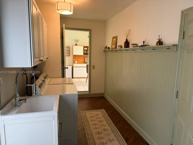 Laundry room featuring beadboard wall paneling, herringbone-pattern wood-finish flooring, built-in upper cabinetry, utility sink with a high-arch pull-down faucet, and a ceiling-mounted drum light fixture