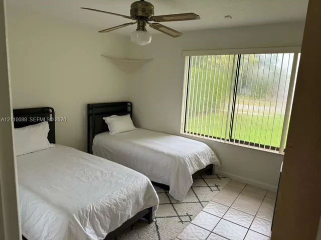 Room featuring neutral-toned walls, tile flooring, a ceiling fan with integrated lighting, and a large horizontal window with vertical blinds