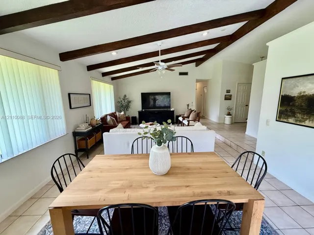 Vaulted ceiling featuring exposed wood beams, neutral ceramic tile flooring, and recessed lighting
