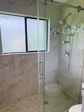 Walk-in shower featuring floor-to-ceiling stone-finish tile, sliding glass door, dual shower heads, decorative mosaic tile inlay, and integrated bench seating