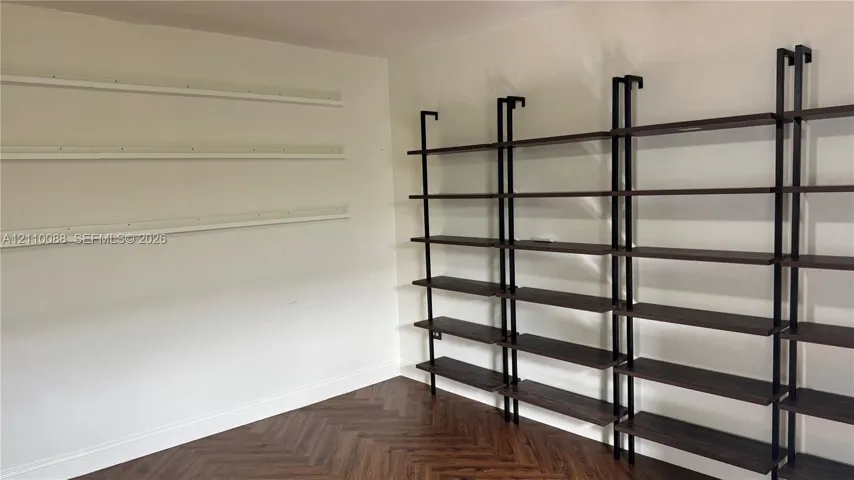 Herringbone wood-finish flooring featuring floor-to-ceiling dark wood-finish shelving with black metal supports, complemented by wall-mounted horizontal shelving