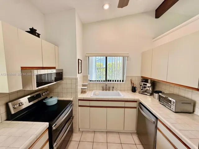 Kitchen featuring flat-panel cabinetry, tiled countertops, a recessed apron-front sink, stainless steel appliances, and vaulted ceilings with exposed structural beams