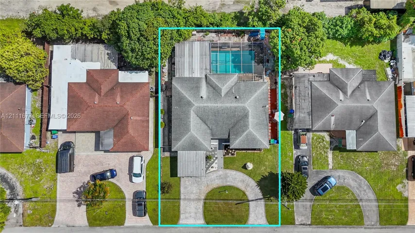 Aerial view featuring a screened-in swimming pool, a multi-section roof, and a paved circular driveway
