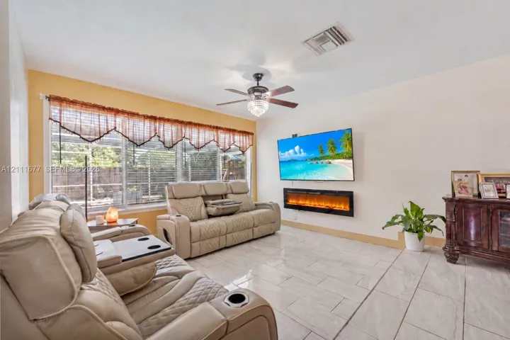 Living area featuring large format tile flooring, a wall-mounted electric fireplace, and a ceiling fan with integrated lighting