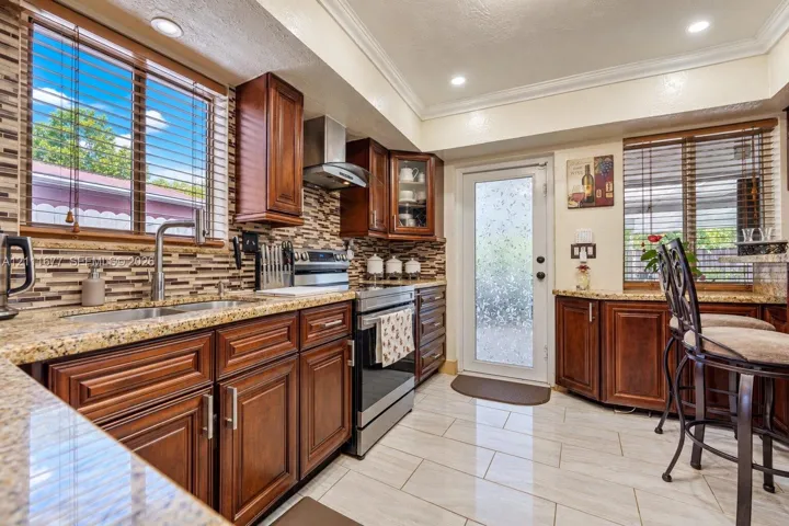 Kitchen featuring dark wood cabinetry, stone countertops, a mosaic tile backsplash, stainless steel appliances, and tile flooring