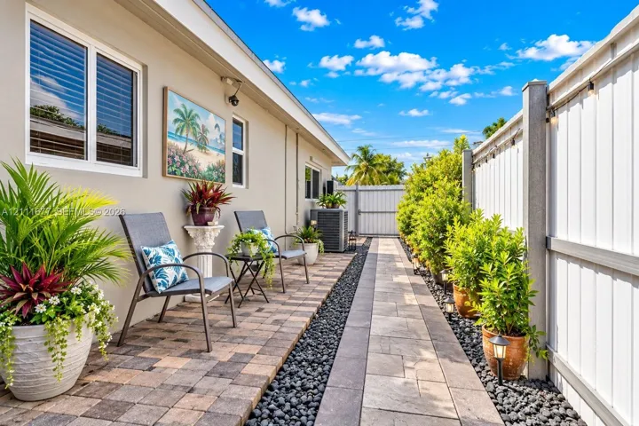 Exterior side yard featuring multi-toned paver hardscaping, decorative stone border, and a privacy fence