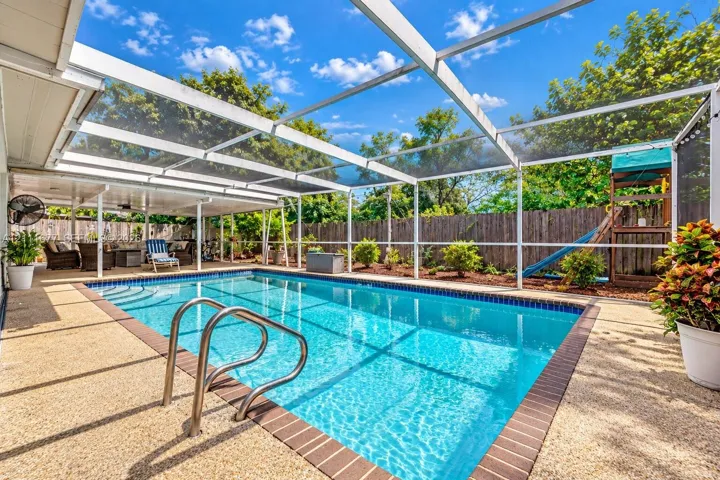 Screened-in pool area featuring a pebble-finish pool deck, brick coping, stainless steel ladder, and a covered lanai