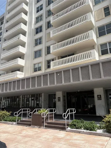 High-rise exterior featuring private balconies with decorative railings, a prominent facade with structured concrete detailing, and a ground-level entryway with stone-clad columns