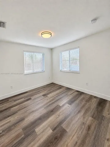 Room featuring wood-finish flooring, dual windows with blinds, and a central flush-mount light fixture