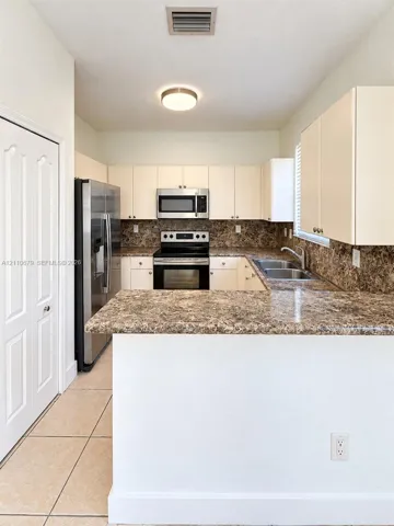 Kitchen featuring solid-surface countertops, stainless steel appliances, flat-panel cabinetry, and tile flooring
