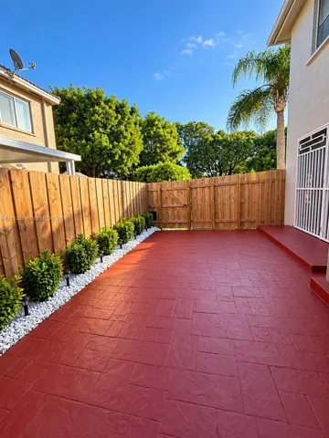 Stamped concrete patio featuring a perimeter of white decorative stones, integrated shrubbery, a wood privacy fence, and a metal security door