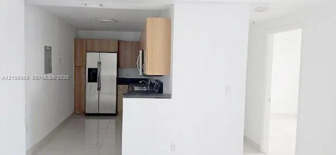 Kitchen featuring light wood-finish cabinetry, stainless steel refrigerator, stone-finish countertops, and tile flooring