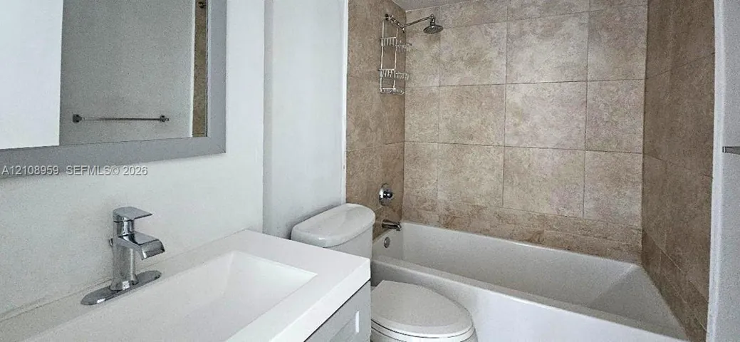 Bathroom featuring a vanity with a rectangular basin, chrome faucet, large rectangular mirror, and a tub-shower combination with floor-to-ceiling stone-look wall tiling