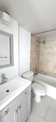 Bathroom featuring a grey vanity with an integrated rectangular sink, stone-finish wall tile in the shower enclosure, a chrome shower fixture, and tile flooring